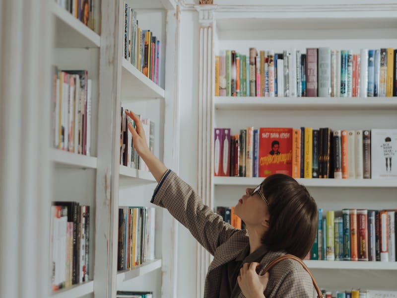 Mujer buscando libros entre estantería de biblioteca