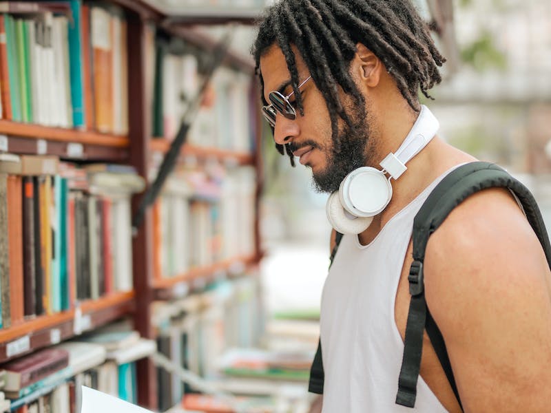 Joven con ropa de deporte buscando libros en un estante en biblioteca